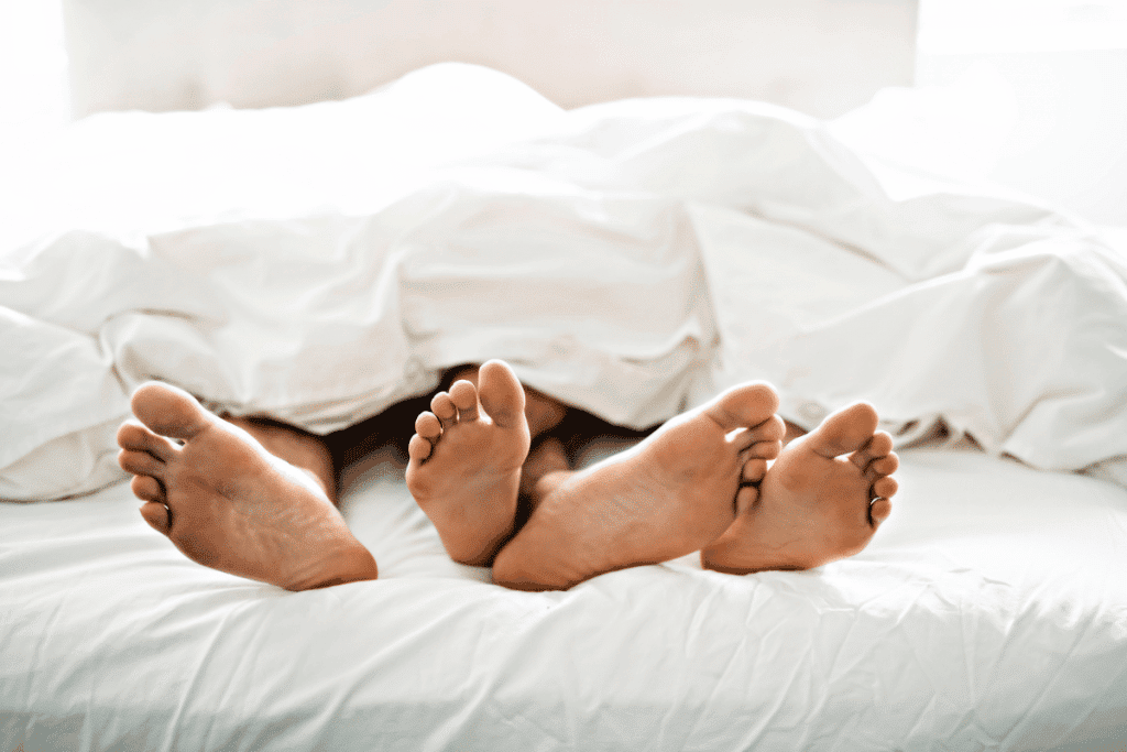 Zwei rissige Füße, die unter der Bettdecke liegen